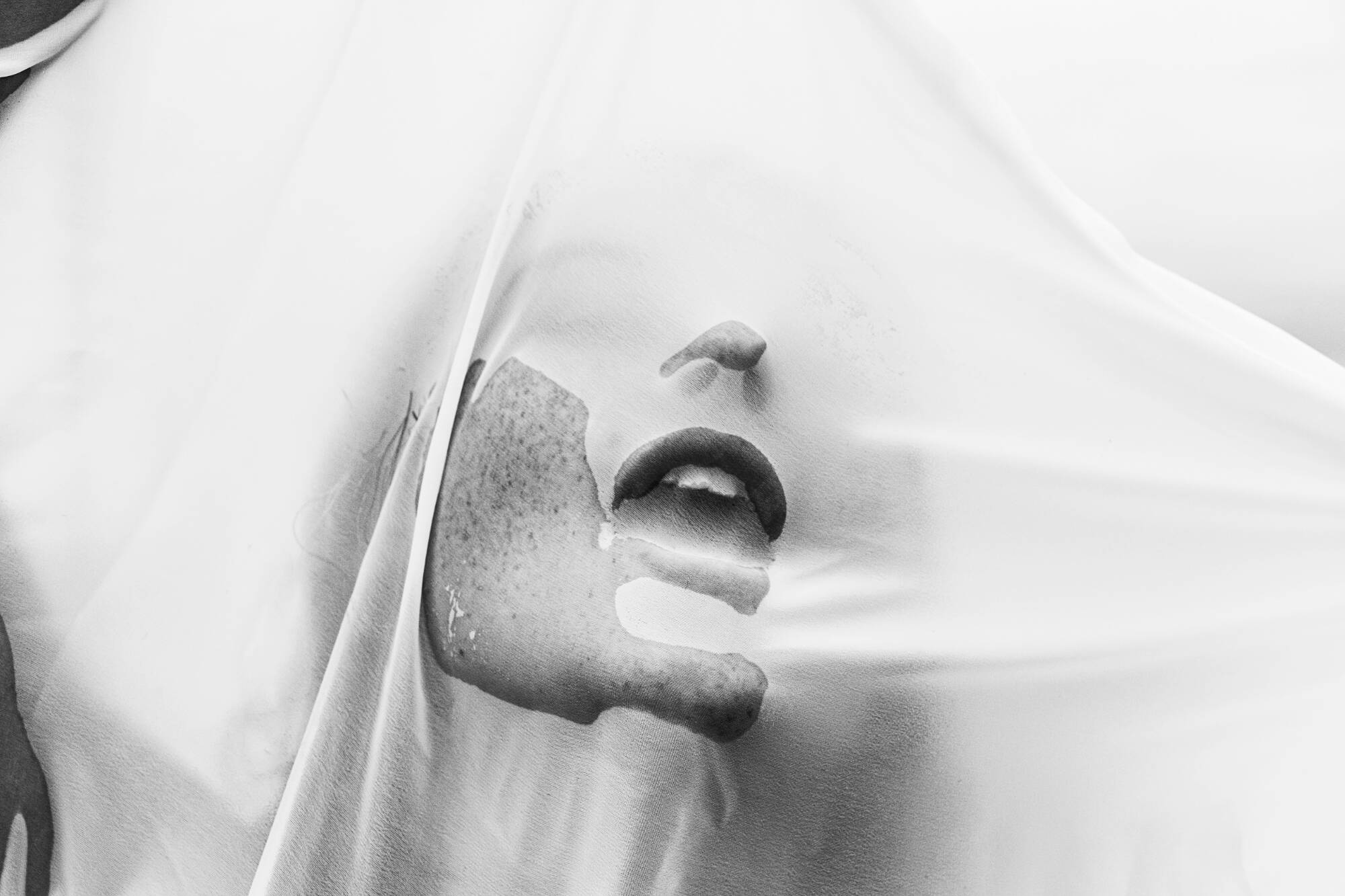Black and white digital photograph of a woman pressing her face against a sheer, wet, cloth.